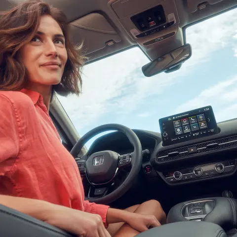 Žena sediaca na sedadle vodiča a ovládajúca obrazovku systému infotainment vozidla Honda ZR-V Hybrid.