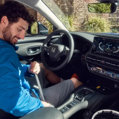 Muž na sedadle vodiča si zapína bezpečnostný pás vo vozidle Honda ZR-V Hybrid. 