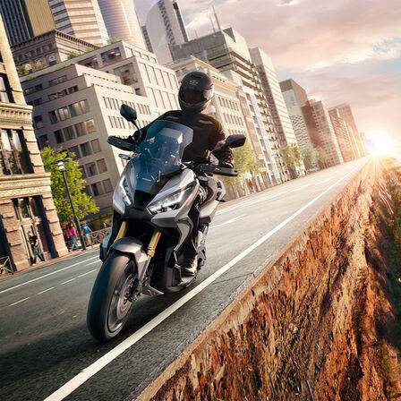 Honda X-ADV – trojštvrťový záber spredu na stroj s jazdcom, medzi mestom a lesom, sivý motocykel