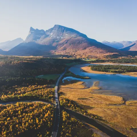 Klasický škandinávsky pohľad na horskú krajinu s cestou, horami a fjordom s modrou oblohou v lete, severné Nórsko, kraj Finnmark, záber z dronu