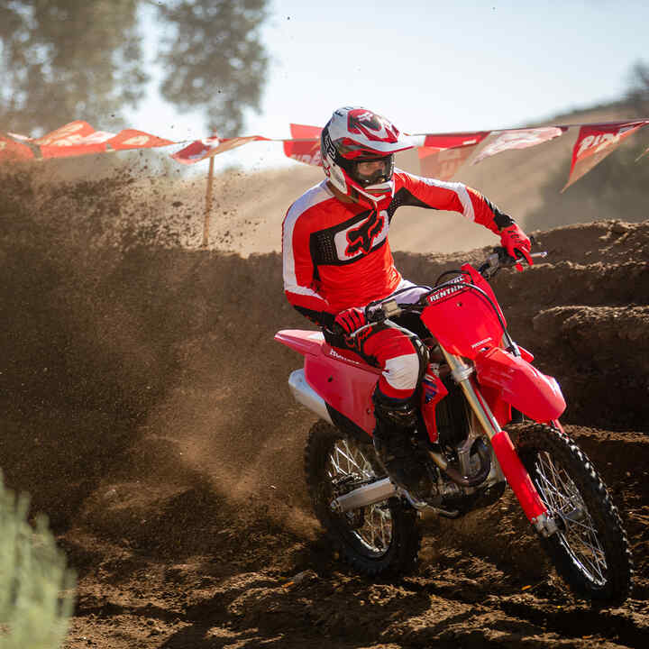 Model Honda CRF450R pri jazde v teréne s horami v pozadí.