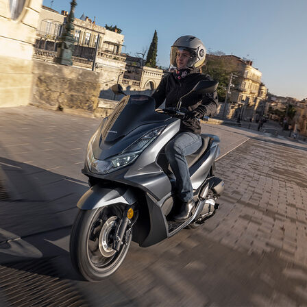 Honda PCX125 s mestom na pozadí