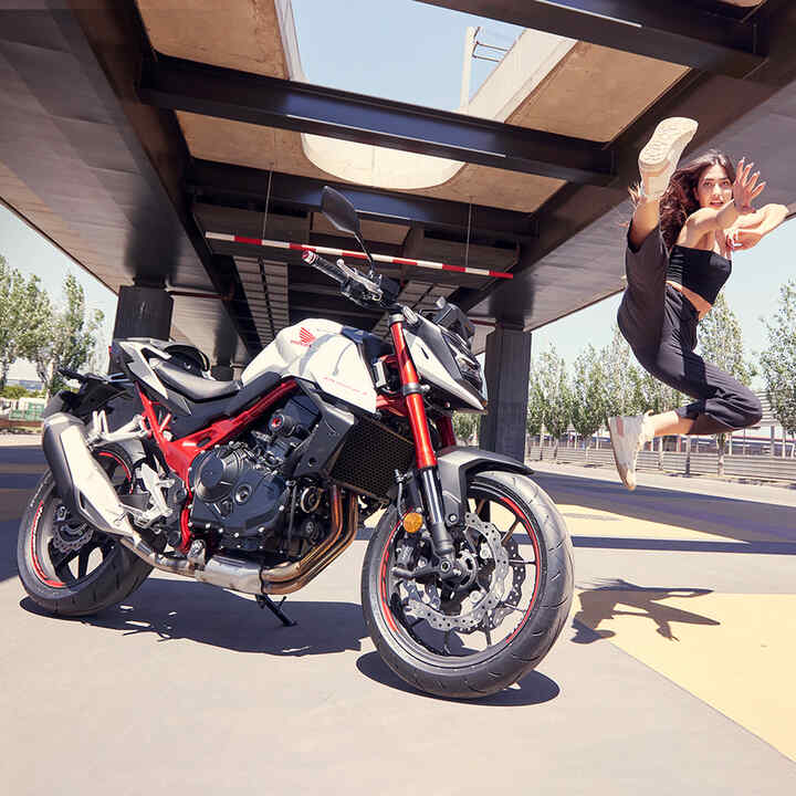Tanečnica skákajúca vo vzduchu vedľa modelu Honda CB750 Hornet.