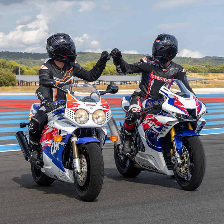 Záber spredu na dvoch jazdcov sediacich na motocykloch Honda Fireblades, ktorí si blahoželajú päsťami na pretekárskej trati.